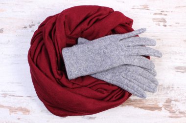 Pair of woolen gloves and shawl for woman on old wooden background