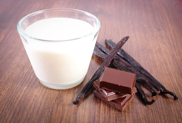 Chocolate negro, palitos de vainilla fragantes y un vaso de leche en tablón de madera — Foto de Stock