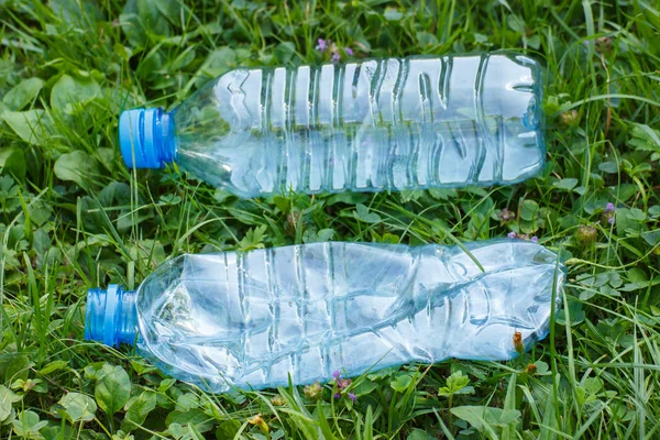 Plastic bottles of mineral water on grass in park, littering of environment — Stock Photo, Image