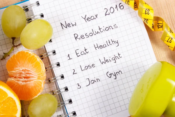 New years resolutions written in notebook and fruits, dumbbells with centimeter — Stockfoto