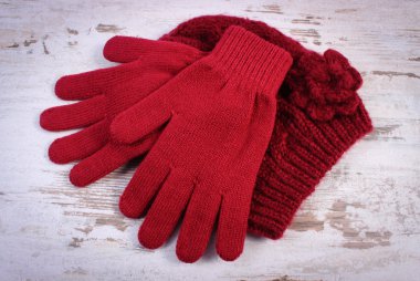 Pair of woolen gloves and cap for woman on old wooden background