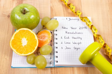 New years resolutions written in notebook and fruits, dumbbells with centimeter