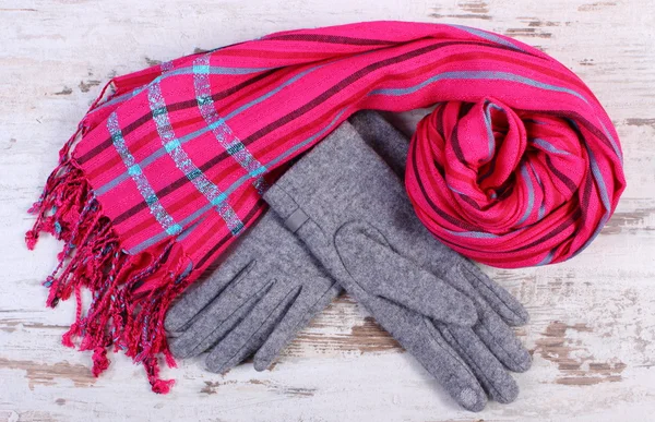 Pair of woolen gloves and shawl for woman on old wooden background