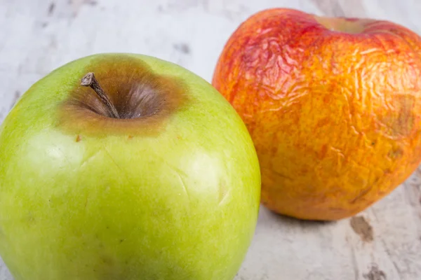 Spoiled apple on old wooden white table — Stock Photo, Image