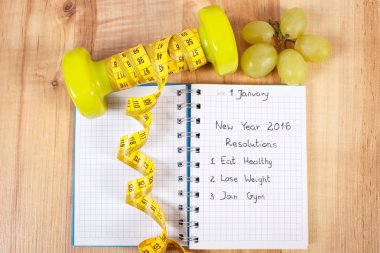 New years resolutions written in notebook and dumbbells with centimeter