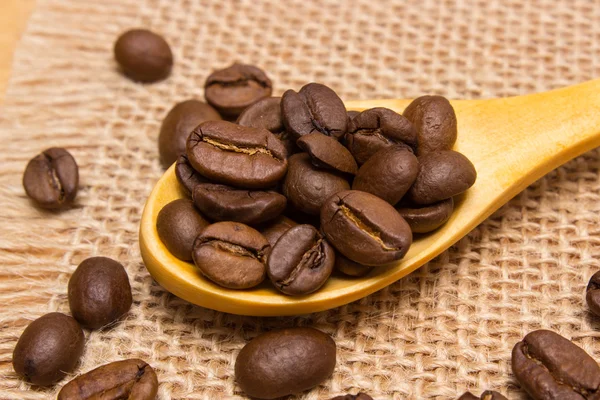 Haufen Kaffeebohnen mit Holzlöffel auf Jutescreme — Stockfoto