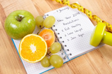 New years resolutions written in notebook and fruits, dumbbells with centimeter