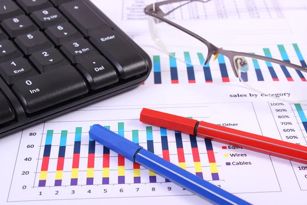 Penna, occhiali e tastiera del computer sul grafico finanziario, concetto di business — Foto Stock