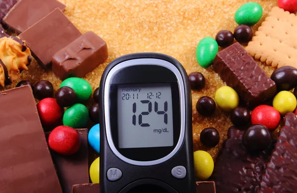 Glucosímetro con un montón de dulces y azúcar morena de caña, alimentos poco saludables — Foto de Stock