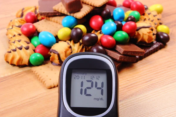 Glucometer with heap of sweets on wooden surface, diabetes and unhealthy food — Stock Photo, Image