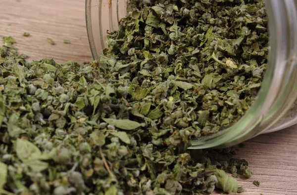 Dried marjoram spilling out of glass jar. Wooden background — Stock Photo, Image