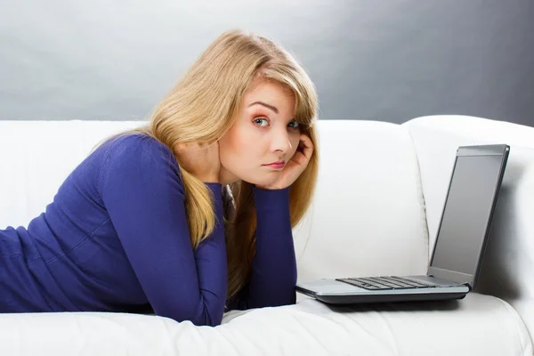Грустная женщина лежит на диване и с помощью ноутбука, современные технологии — стоковое фото