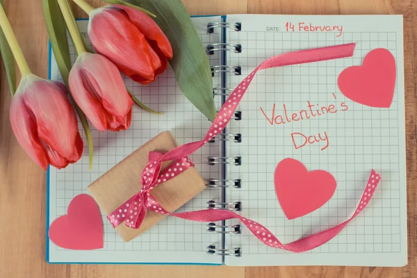 Jahrgangsfoto, Valentinstag in Notizbuch geschrieben, frische Tulpen, verpacktes Geschenk und Herzen, Dekoration für Valentinstage — Stockfoto