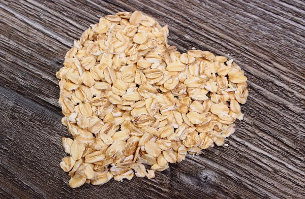 Heart of oat flakes on wooden background — Stock Photo, Image