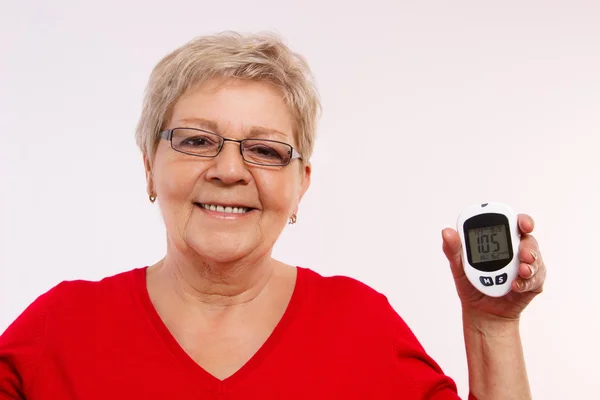 Счастливая пожилая женщина держит глюкометр, измерения и проверки уровня сахара, концепция диабета в старости — стоковое фото