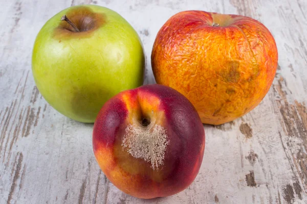 Испорченный персик и яблоко на старом деревянном белом столе — стоковое фото