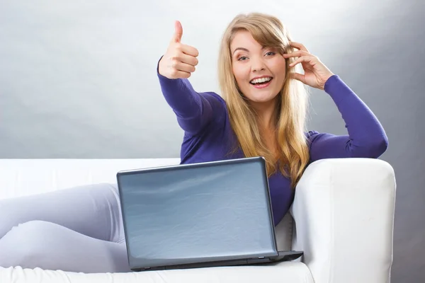 Mujer feliz con el ordenador portátil sentado en el sofá y mostrando pulgares hacia arriba, la tecnología moderna — Foto de Stock