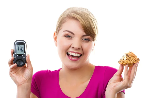 Mulher feliz segurando glicosímetro e cupcake fresco, medindo e verificando o nível de açúcar, conceito de diabetes — Fotografia de Stock