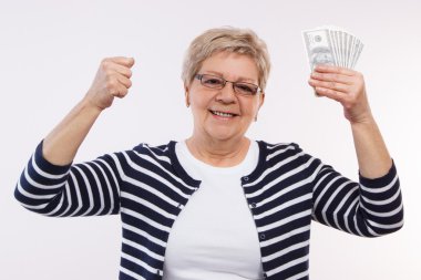 Happy senior female holding currencies dollar and clenching her fist, concept of financial security in old age