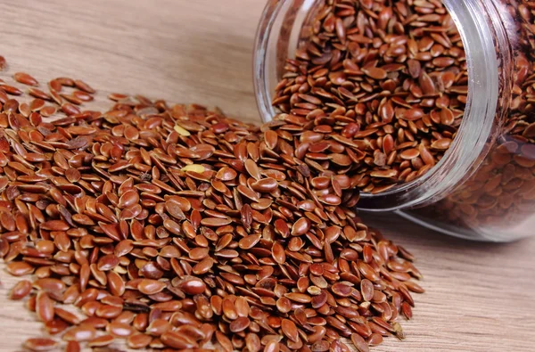 Linseed spilling out of jar on wooden background — Stock Photo, Image