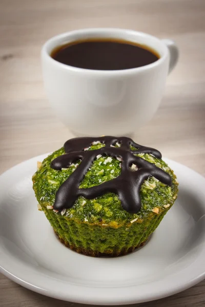 Frischer Muffin mit Spinat, getrockneter Kokosnuss, Schokoglasur und Tasse Kaffee, leckeres gesundes Dessert — Stockfoto
