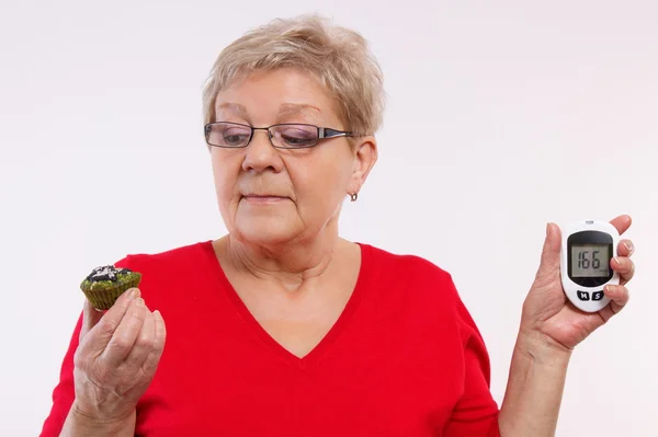 Mujer mayor sorprendida sosteniendo glucosímetro y magdalena fresca, midiendo y comprobando el nivel de azúcar, concepto de diabetes — Foto de Stock