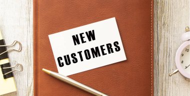 Not defterinin üzerinde duran beyaz kart üzerinde NEW CUSTOMERS metni.