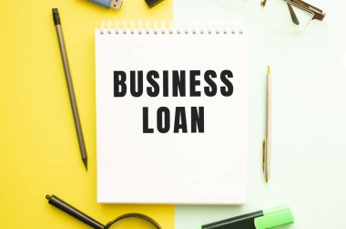 Ofis masasında ofis malzemeleriyle birlikte BUSINESS kredisinin olduğu defter. Sarı arkaplan kavramı. İş konsepti.