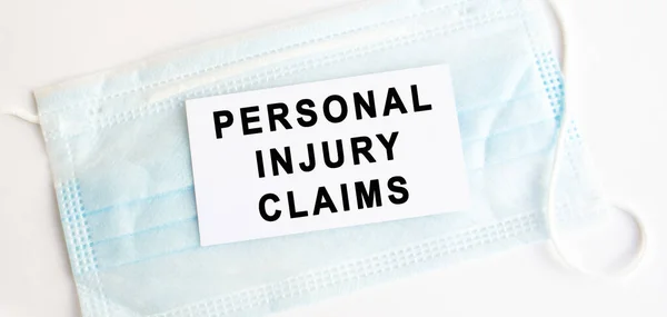 White card with the inscription PERSONAL INJURY CLAIMS on a medical protective mask. Medical concept.