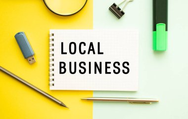 Ofis masasında ofis malzemeleriyle birlikte LOCAL İŞ mesajı olan bir defter. Sarı arkaplan kavramı. İş konsepti.