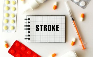 Beyaz arkaplanda STROKE mesajı olan not defteri. Yakınlarda çeşitli ilaçlar var. Tıbbi konsept.