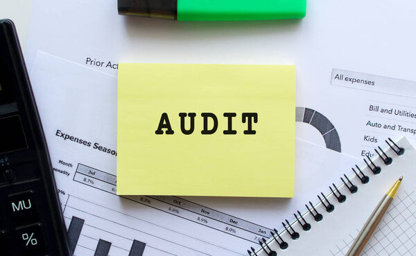 Notepad with text AUDIT on a white background, near office supplies, pen and calculator.