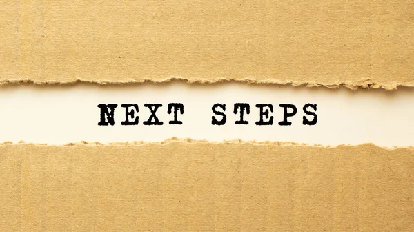 Yırtık kahverengi kağıdın arkasında görünen NEXT STEPS metni.