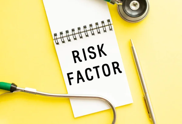 Text RISK FACTOR on notebook with stethoscope and pen on yellow background. Medical concept.