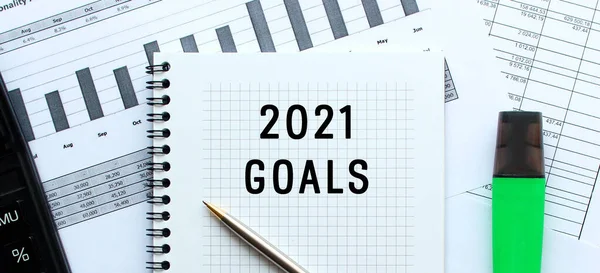 Ofis masasındaki mali tabloların üzerinde duran not defterinin sayfasında 2021 sayılı mesaj var. Hesap makinesinin yanında. İş konsepti.
