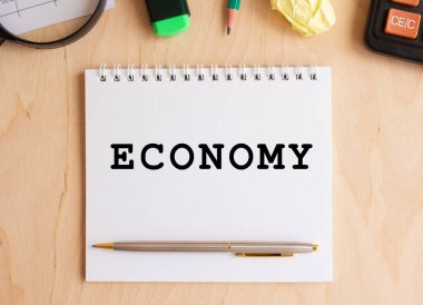 Hesap makinesi ve ofis malzemelerinin yanında, ahşap bir masanın üzerinde ECONOmy mesajı olan not defteri. İş konsepti.