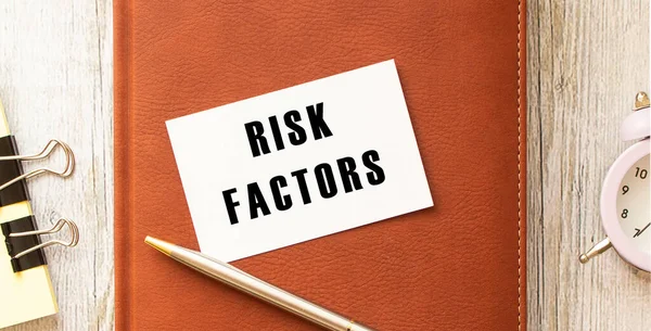 名片一张木制桌子上印有Risk Factors字样 棕色的日记本和钢笔 业务概念 — 图库照片