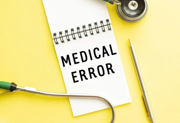 MEDICAL ERROR is written in a notebook on a color table next to pen and a stethoscope. Medical concept