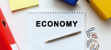 Beyaz arkaplan, belge dizini ve ofis malzemelerinin yanında ECONOmy metni bulunan not defteri.