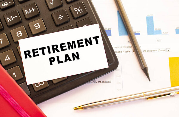 Text RETIREMENT PLAN on white card with metal pen, calculator and financial charts.