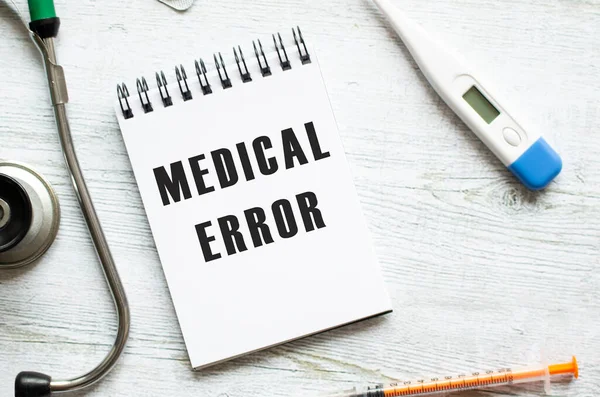 MEDICAL ERROR is written in a notebook on a wooden table next to stethoscope.