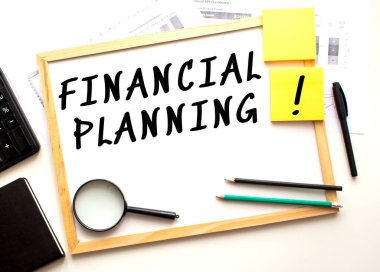 Finans Planlama metni beyaz bir ofis tahtasına yazılmıştır. Ofis malzemeleriyle birlikte çalışma masası. İş ve mali konsept.