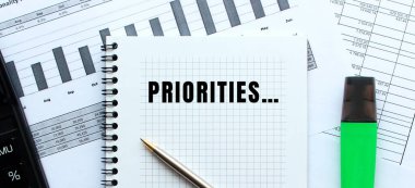 Ofis masasındaki mali tabloların üzerinde duran bir not defterinin sayfasına özel metinler yaz. Hesap makinesinin yanında. İş konsepti.