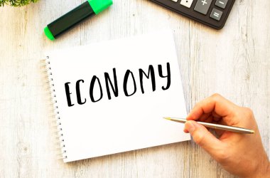 Kalemli bir el, ahşap bir masanın üzerindeki deftere ECONOmy metni yazar. Yukarıdan bak. İş konsepti.