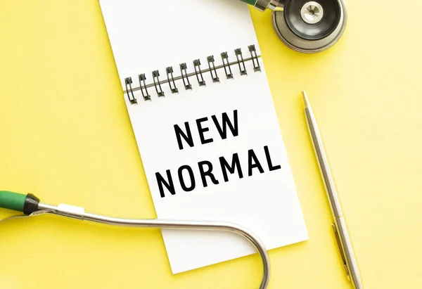 NEW NORMAL, kalem ve steteskopun yanındaki renk masasının üzerindeki bir deftere yazılmıştır. Tıbbi konsept