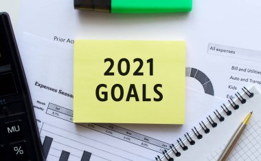 Ofis masasındaki mali tabloların üzerinde duran not defterinin sayfasında 2021 sayılı mesaj var. Hesap makinesinin yanında. İş konsepti.