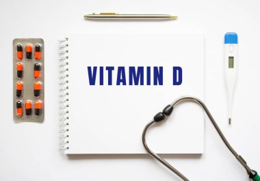 VITAMIN D, ilaç ve steteskopun yanındaki beyaz bir masanın üzerine yazılmış bir defter. Tıbbi konsept