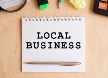 Hesap makinesi ve ofis malzemelerinin yanında, ahşap bir masanın üzerinde LOCAL BUSINESS yazılı not defteri. İş konsepti.