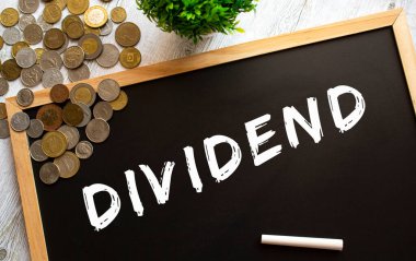 Üzerinde DIVIDEND yazılı karatahta ve gri ahşap bir masada metal paralar. Mali konsept.