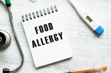 FOOD ALLERJİ, steteskopun yanındaki açık tahta bir masanın üzerine yazılmış bir defter. Tıbbi konsept